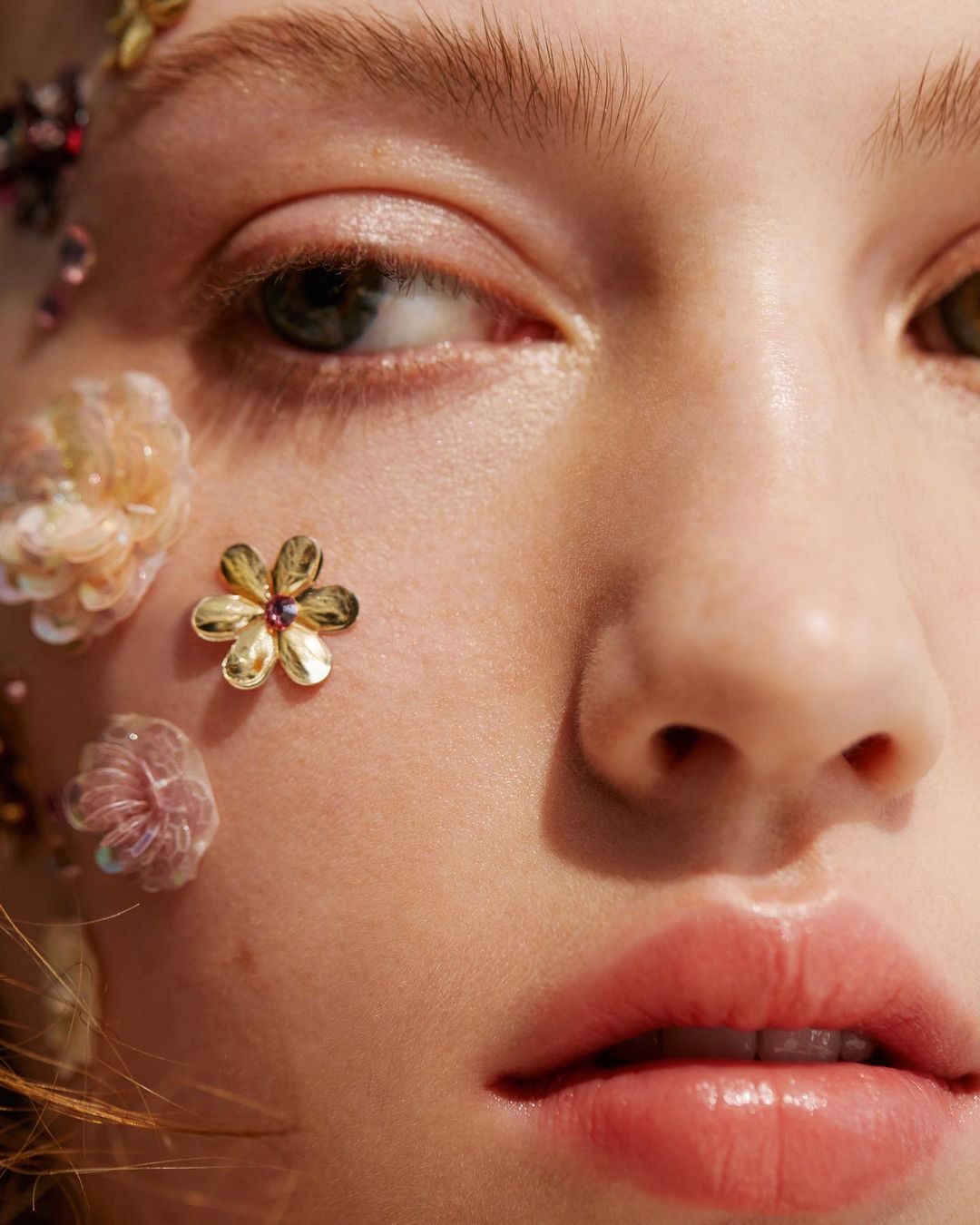 Close-up portrait of a woman's face with fair skin adorned with gold and iridescent floral embellishments highlighting beauty and skincare.