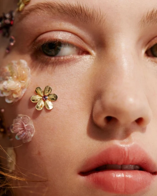 Close-up portrait of a woman's face with fair skin adorned with gold and iridescent floral embellishments highlighting beauty and skincare.