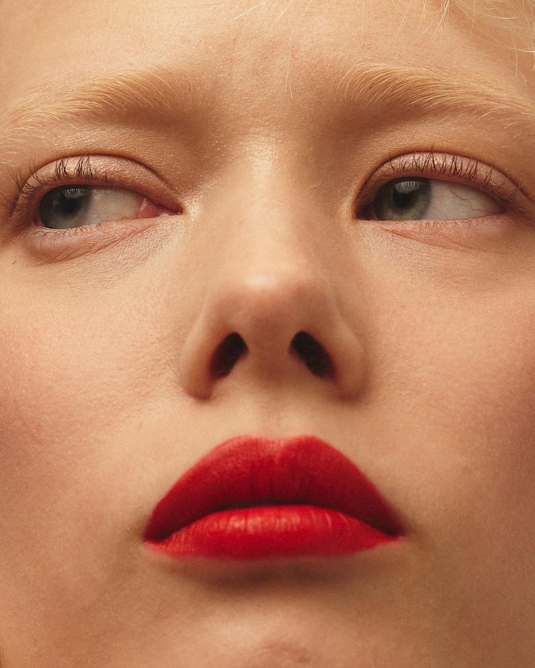 Close-up portrait of a fair-skinned young adult woman with platinum blonde hair and bright red lipstick looking off to the side.