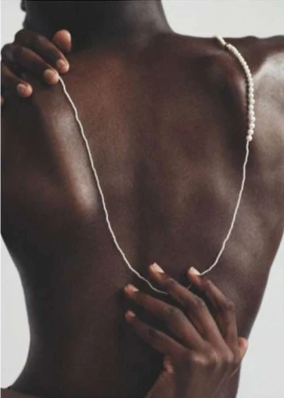 Close-up portrait of a Black person's back draped with a delicate pearl necklace, photographed by Nadia Ryder.