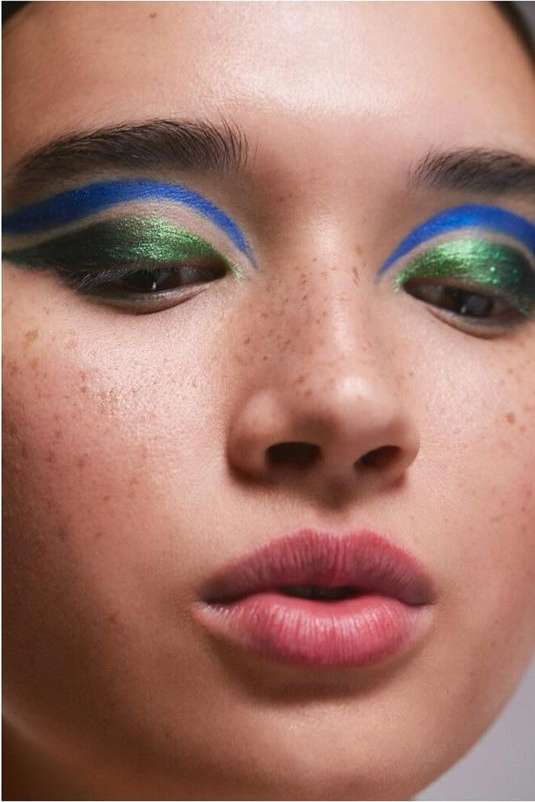 Close-up beauty portrait of a woman with green eyeshadow, blue eyeliner, and freckles photographed by Nadia Ryder