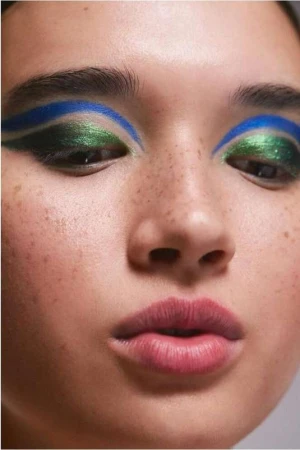 Close-up beauty portrait of a woman with green eyeshadow, blue eyeliner, and freckles photographed by Nadia Ryder