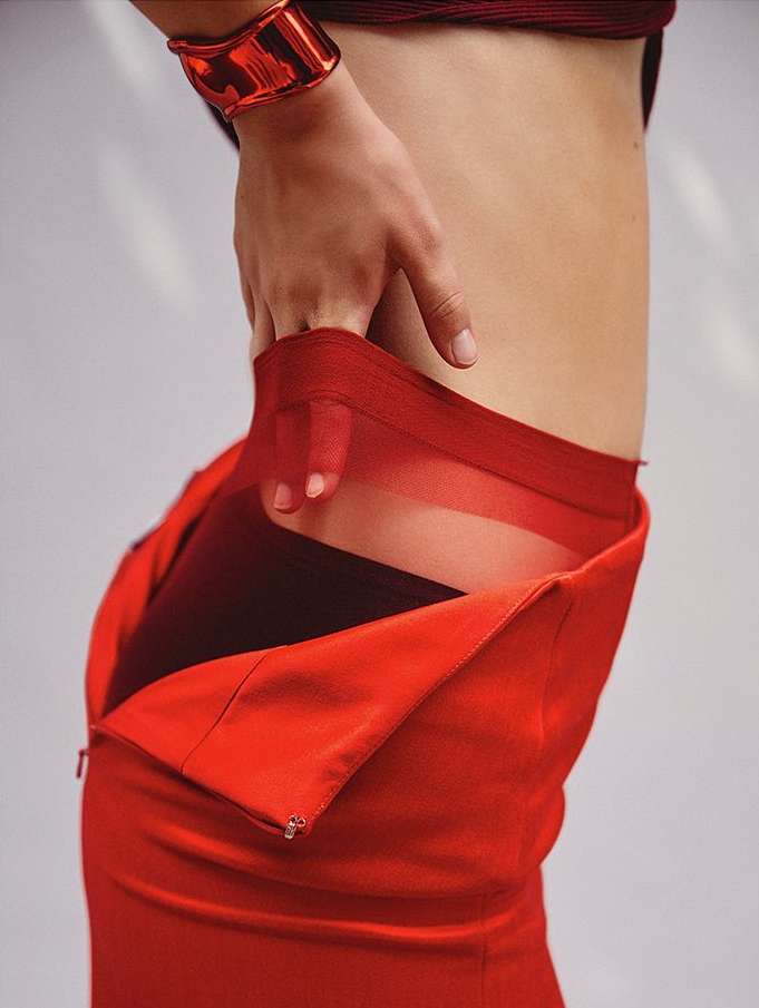 Close-up of a person in a red dress with a large red bangle bracelet, showing the side torso and hand against a neutral backdrop.