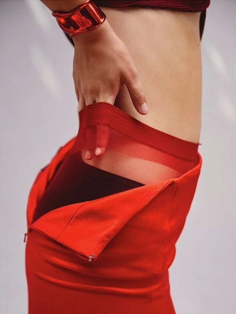 Close-up of a person in a red dress with a large red bangle bracelet, showing the side torso and hand against a neutral backdrop.