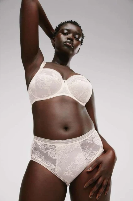 Confident Black woman poses in bra and high-waisted underwear on white background in a low angle shot, showing off lingerie.