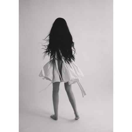Monochrome portrait from the back of a slender woman with long black hair in a white dress against a clean studio backdrop.