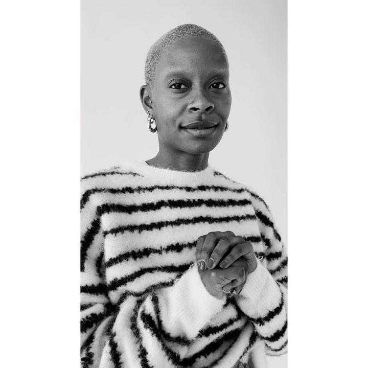 Black woman with short buzzcut wearing a striped sweater, captured in a monochrome portrait.