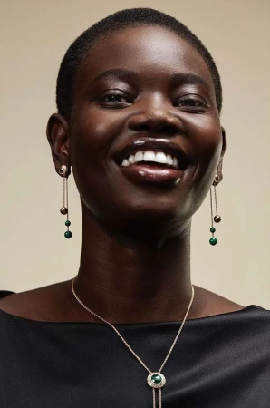 Elegant portrait of a Black woman smiling with dangling earrings and a pendant necklace in a studio setting with a cream background.