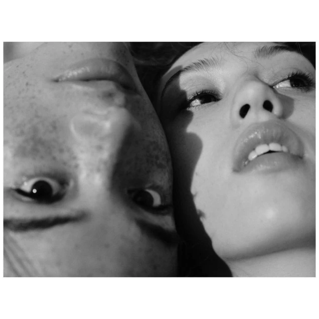Black and white portrait of a woman and a man in close proximity, looking upwards, with shadows partially obscuring the faces.