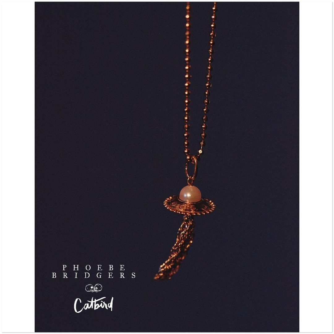 Elegant pearl necklace with a gold chain and tassel against a dark background, featuring the text "Phoebe Bridgers" and "Catbird".
