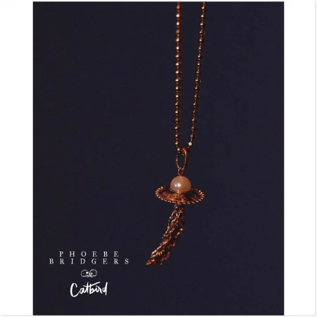 Elegant pearl necklace with a gold chain and tassel against a dark background, featuring the text "Phoebe Bridgers" and "Catbird".