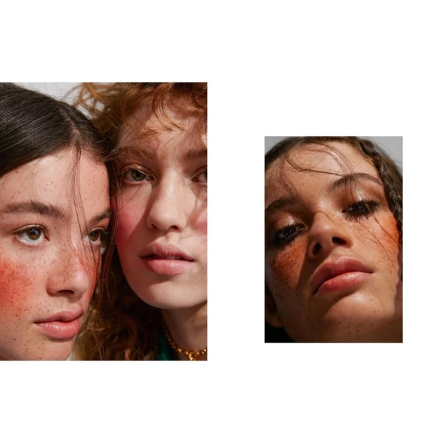 Close-up of two fair-skinned young women with freckles and red makeup, posed in a bright studio setting for a beauty or fashion editorial.