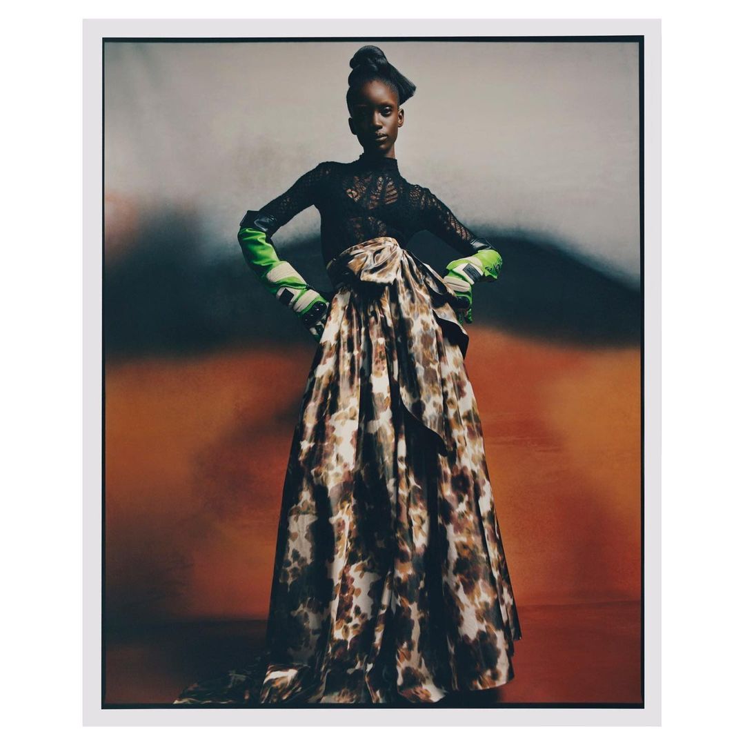 Elegant high-fashion portrait of a Black model wearing a long flowing skirt and black lace top in a studio with mottled backdrop.