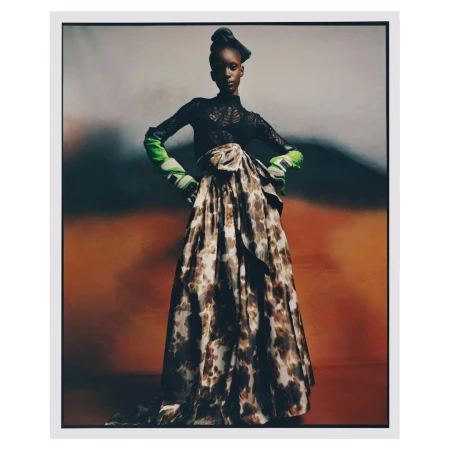 Model in a patterned skirt and black top with green gloves posing against an abstract background by Nadine Ijewere