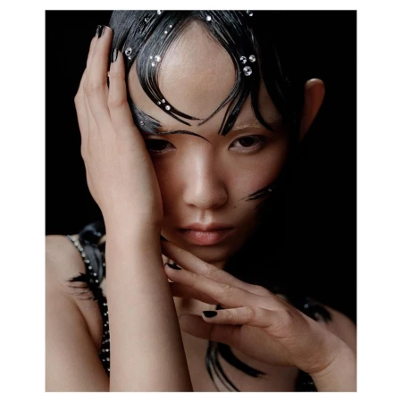 Close-up portrait of an Asian woman with black hair, embellished with shiny jewels, posing against a dark background, and wearing black nail polish.