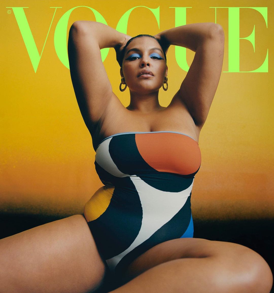 Model wearing a colour-blocked strapless swimsuit with blue eyeshadow against a warm gradient background