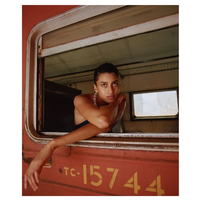 A young woman peers out of a vintage train window, her elegant jewelry catching the light, showcasing classic fashion and travel aesthetics.