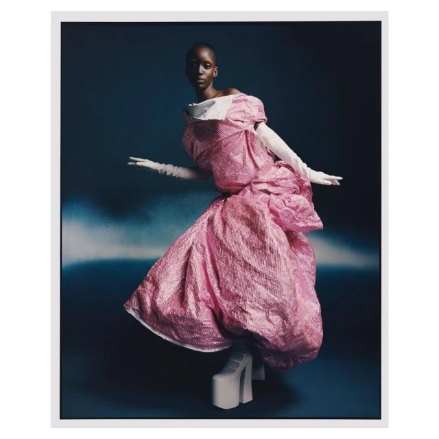 Fashion editorial featuring a Black woman in a pink sequined dress, posed against a blue background. The dress features oversized sleeves.
