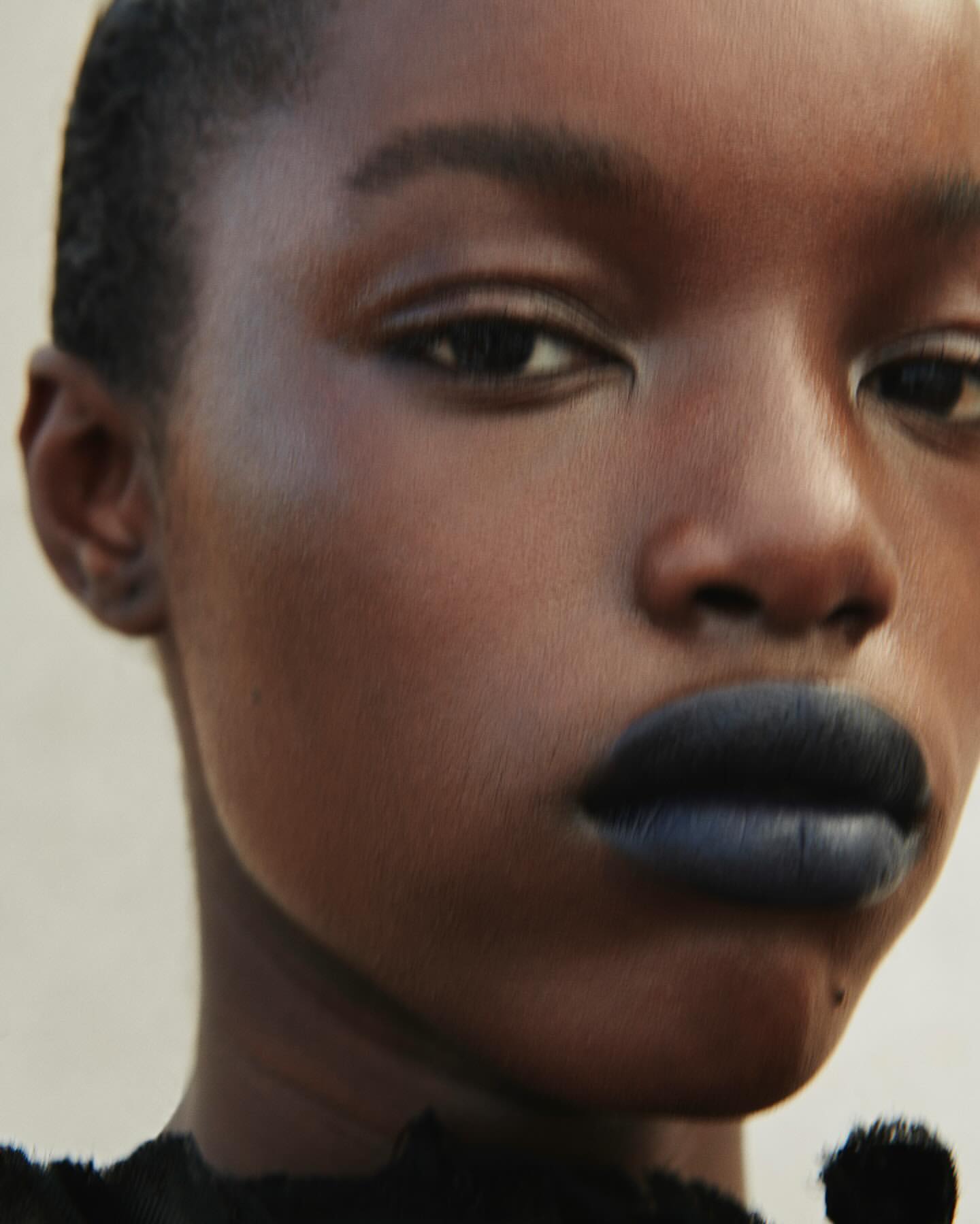 Close-up portrait of a young adult female of African descent wearing dark lipstick against a neutral background in studio lighting.