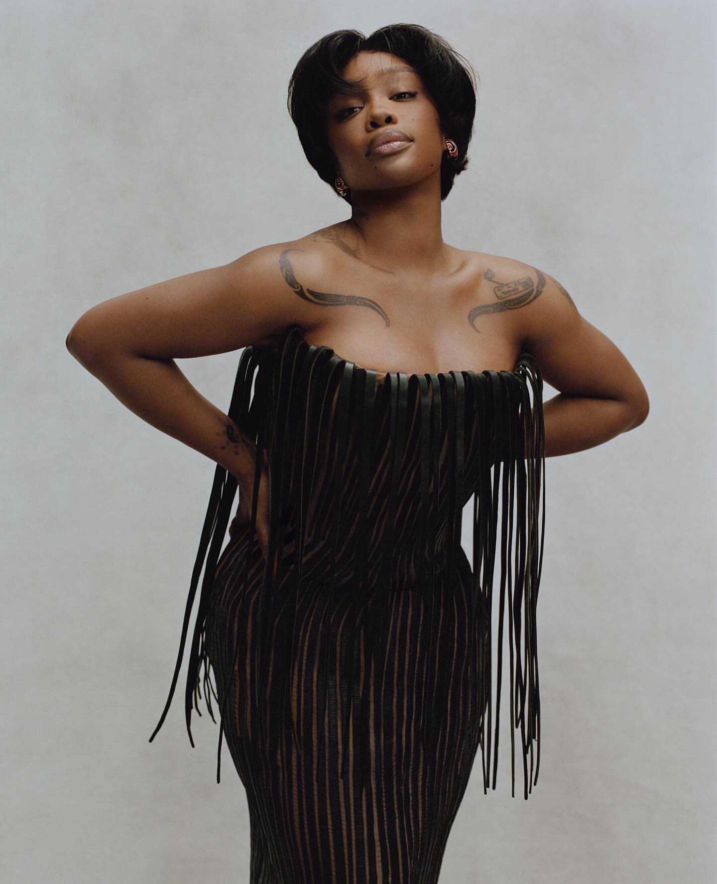 Portrait of SZA in a black fringe dress against a neutral backdrop, showcasing a fashion-forward and elegant studio shot.