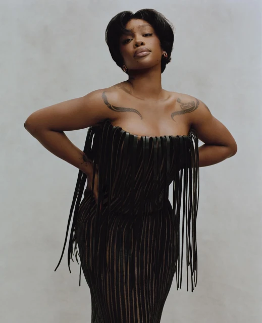 Portrait of SZA in a black fringe dress against a neutral backdrop, showcasing a fashion-forward and elegant studio shot.