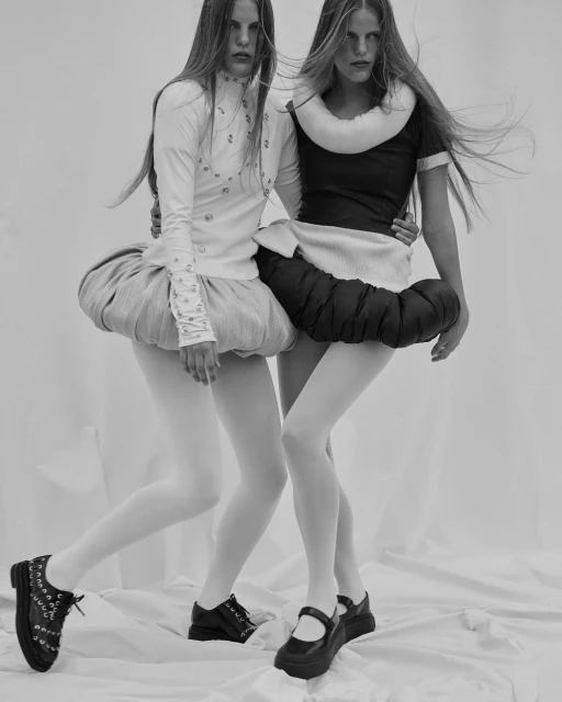Two fashion models strike a pose wearing matching outfits in a monochromatic studio shot showcasing avant-garde style and unique textures.