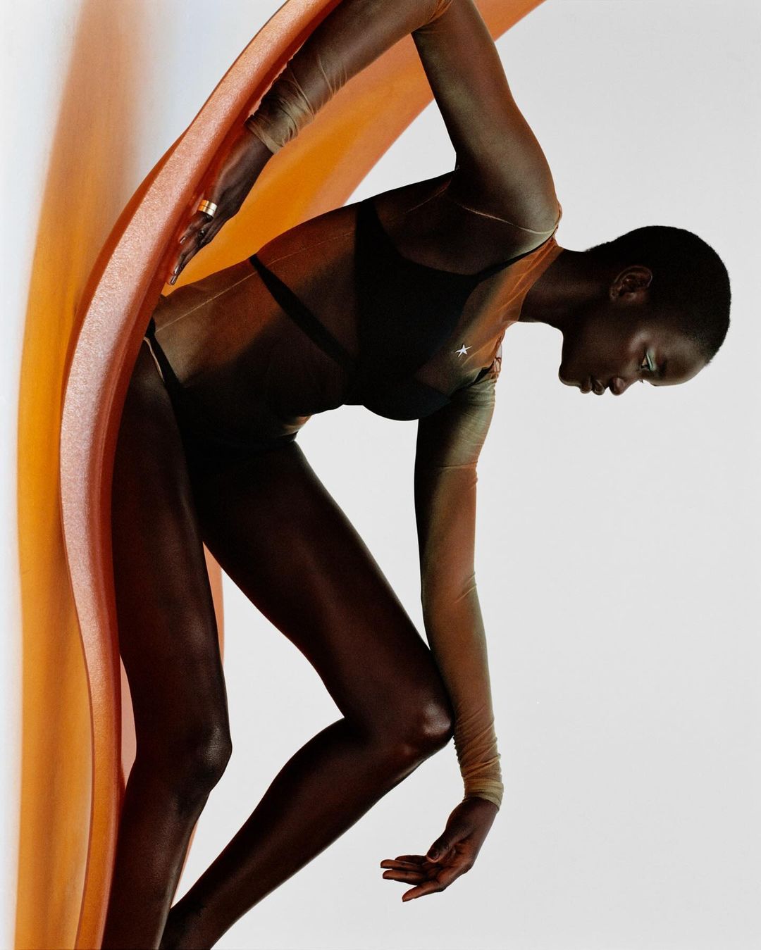 Elegant portrait of a slender African American woman posing in a form-fitting outfit with a flowing orange fabric accent. Beauty fashion photography.
