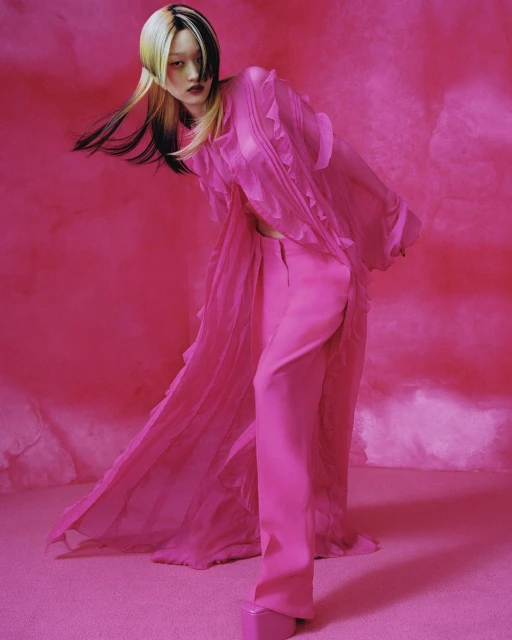Fashionable Asian woman in hot-pink ensemble posing against pink backdrop in studio lighting, showcasing modern, edgy style and bold color.