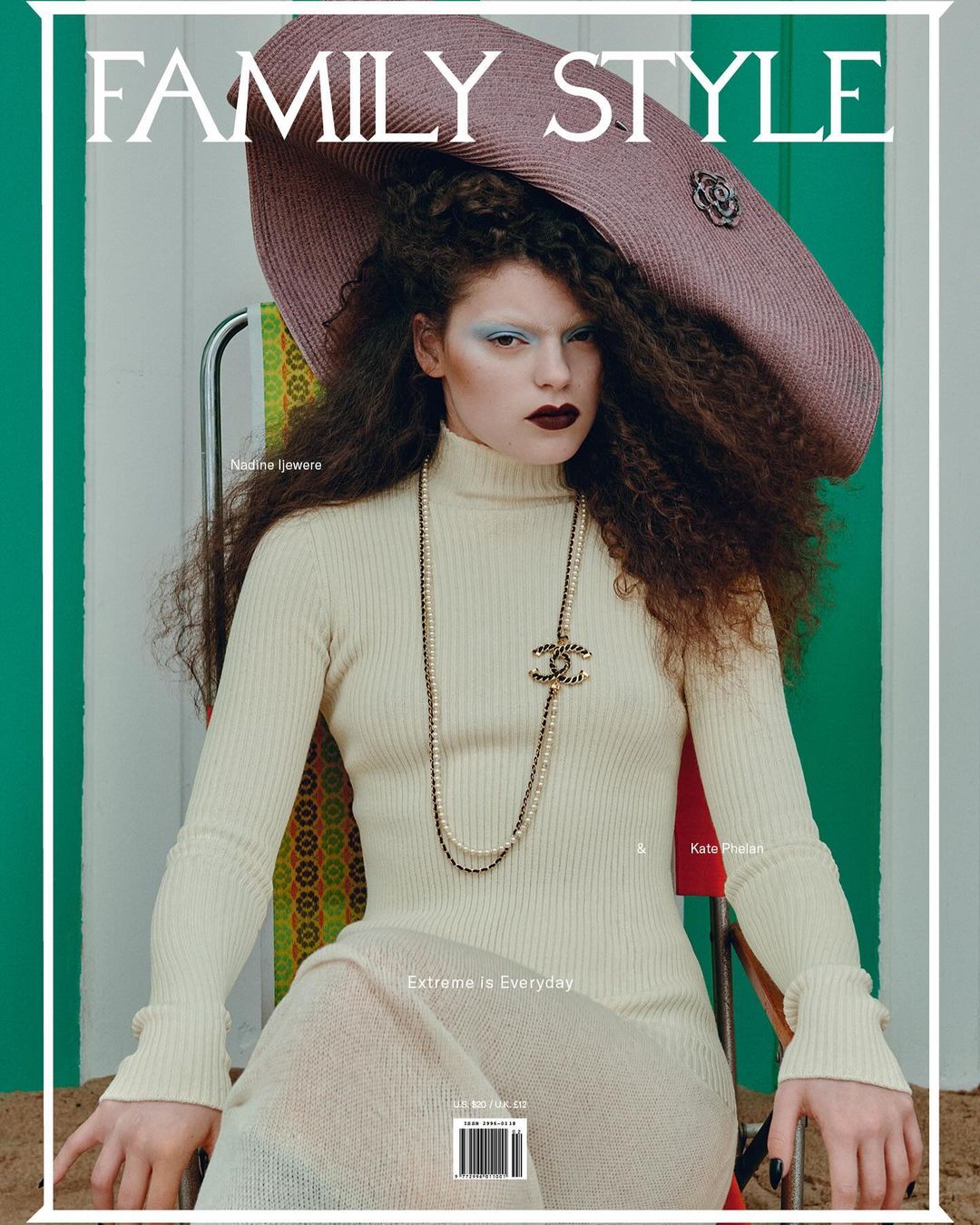 Magazine cover featuring a stylish woman with curly hair, wearing a cream dress, large hat, and a pearl necklace, sitting on a beach chair.