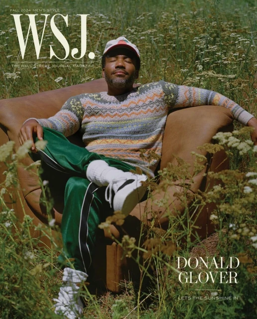 Donald Glover poses on brown leather armchair in a field of flowers for WSJ. Magazine, wearing a patterned sweater and green track pants.
