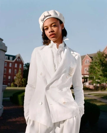 Elegant woman in a white suit and beret poses outdoors against a brick building. Spelman is embroidered on the beret.