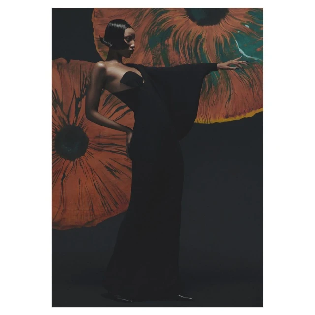 Elegant Black woman in black gown poses against a backdrop of orange flower art. Sophisticated fashion photography in a studio setting.