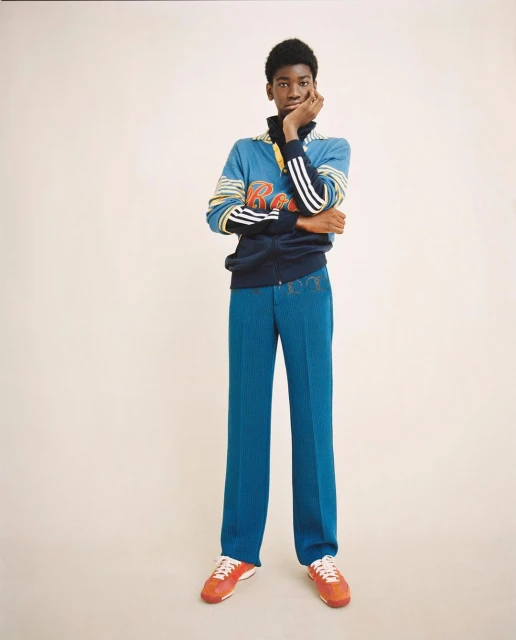 Full-length shot of a young adult in a sporty tracksuit with blue pants and orange sneakers on a neutral background in studio lighting.