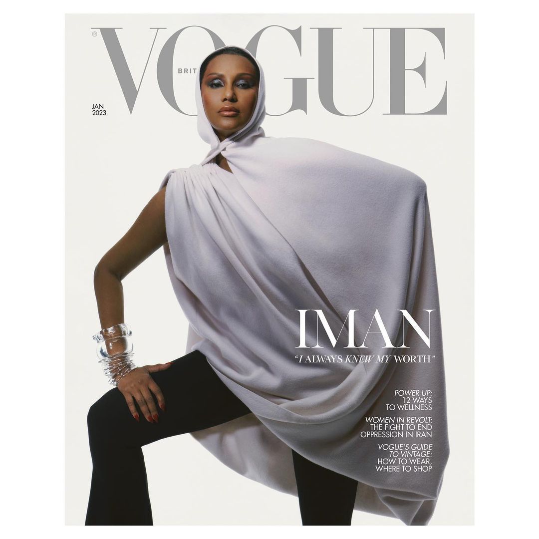 Vogue Britian cover featuring Iman in white hooded cape, black leggings, and silver bracelets, set against a clean white backdrop.