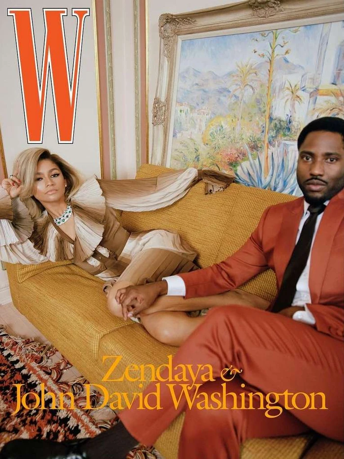 Zendaya and John David Washington seated together on a textured golden yellow sofa in an interior setting.
