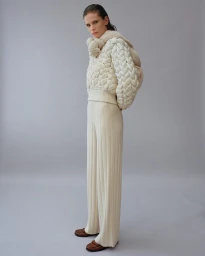 Model in cream chunky knit sweater and matching ribbed trousers standing against grey background