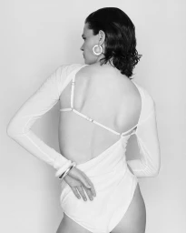 Model with dark wet-look hair wearing a backless white bodysuit and chunky silver hoop earrings and bangles