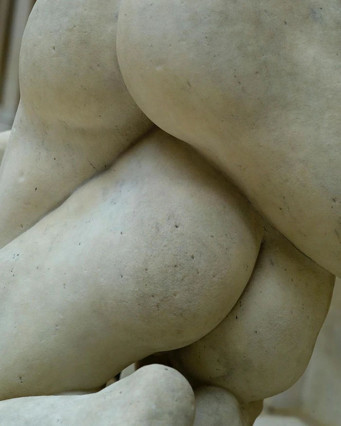 Close-up of a carved stone sculpture depicting a human form, highlighting the smooth marble texture and curved anatomy.