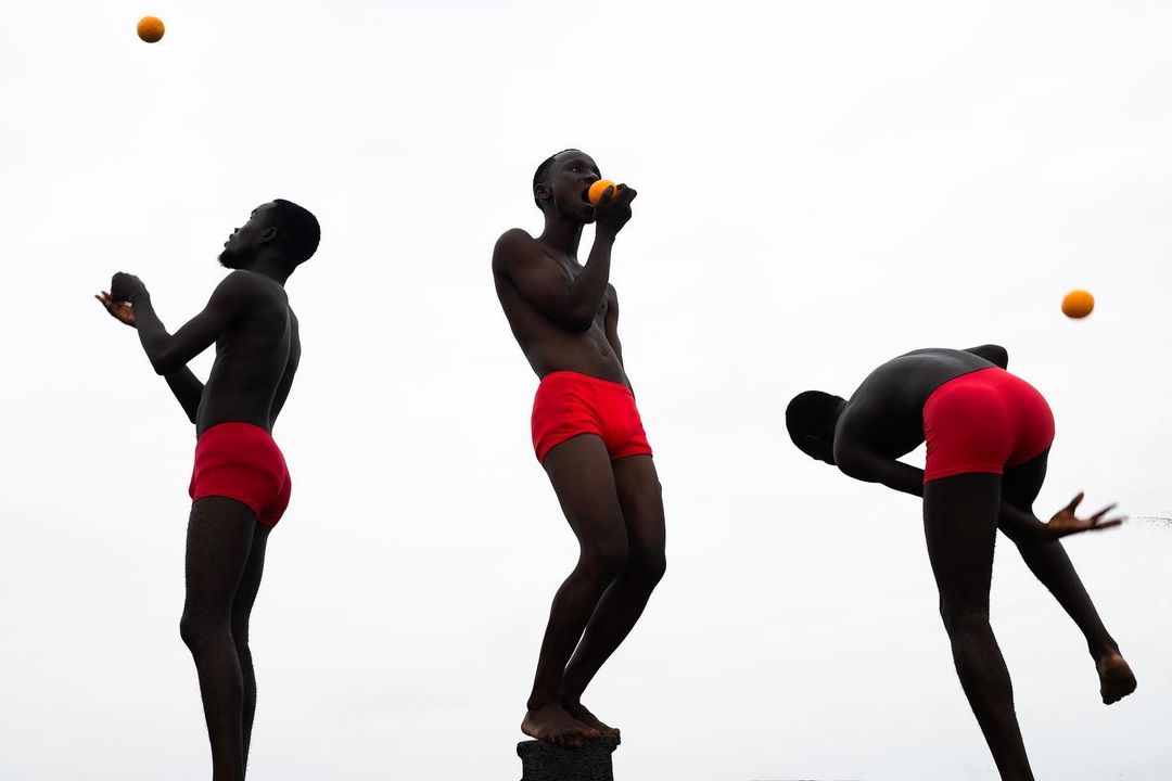 An athletic Black male juggles oranges in three poses against a bright sky, showcasing fitness, coordination, and healthy lifestyle.