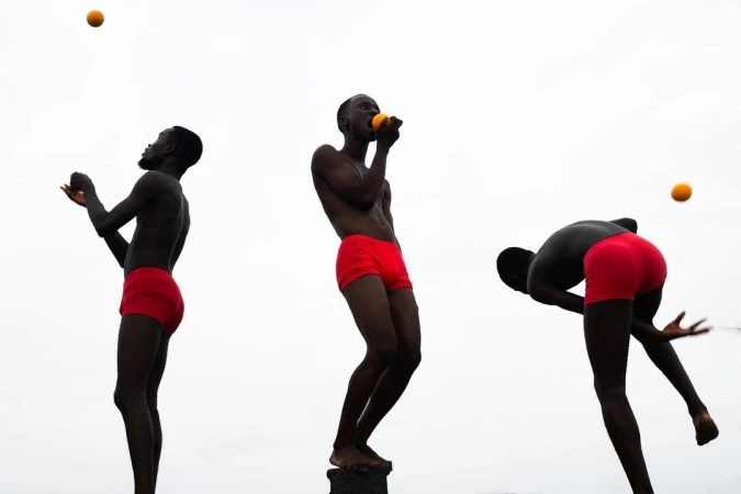 An athletic Black male juggles oranges in three poses against a bright sky, showcasing fitness, coordination, and healthy lifestyle.