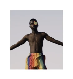 Shirtless black man with arms outstretched wearing multicolored striped shorts and a butterfly over his eye