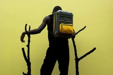 Man wearing a structured hardcase backpack with a yellow pocket, standing against a bright yellow background.