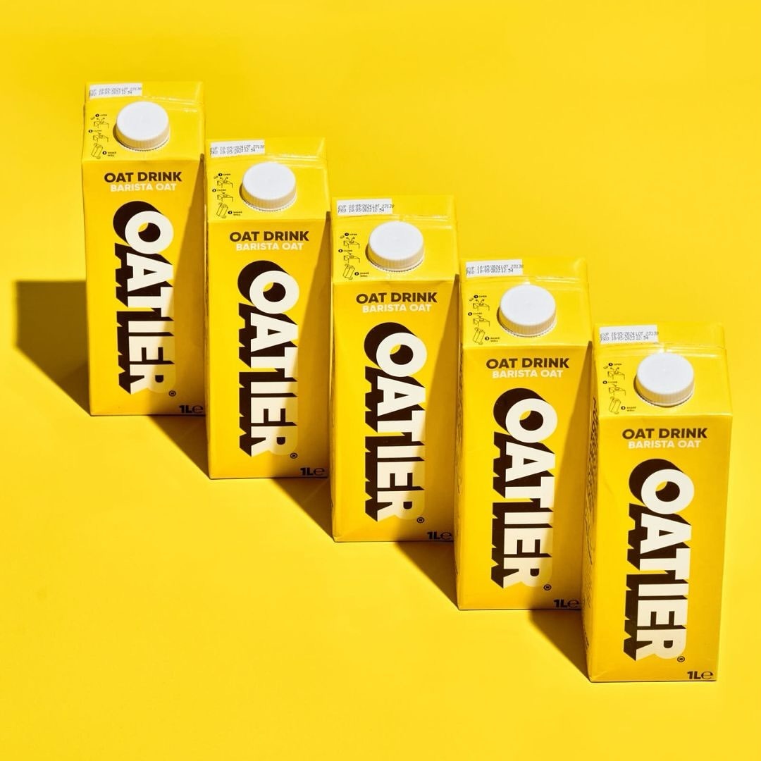 Arrangement of yellow Oatier oat milk cartons in a row, creating a visually appealing and uniform presentation against a yellow backdrop.