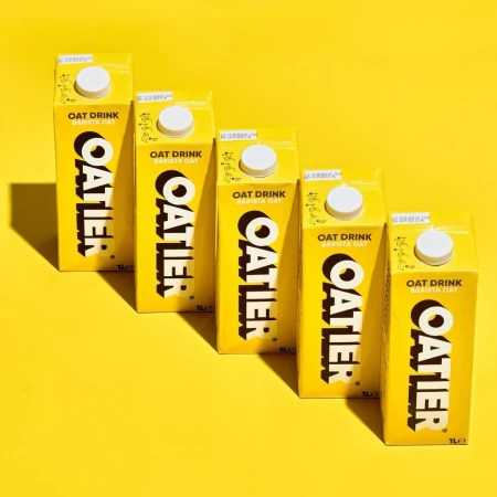 Arrangement of yellow Oatier oat milk cartons in a row, creating a visually appealing and uniform presentation against a yellow backdrop.