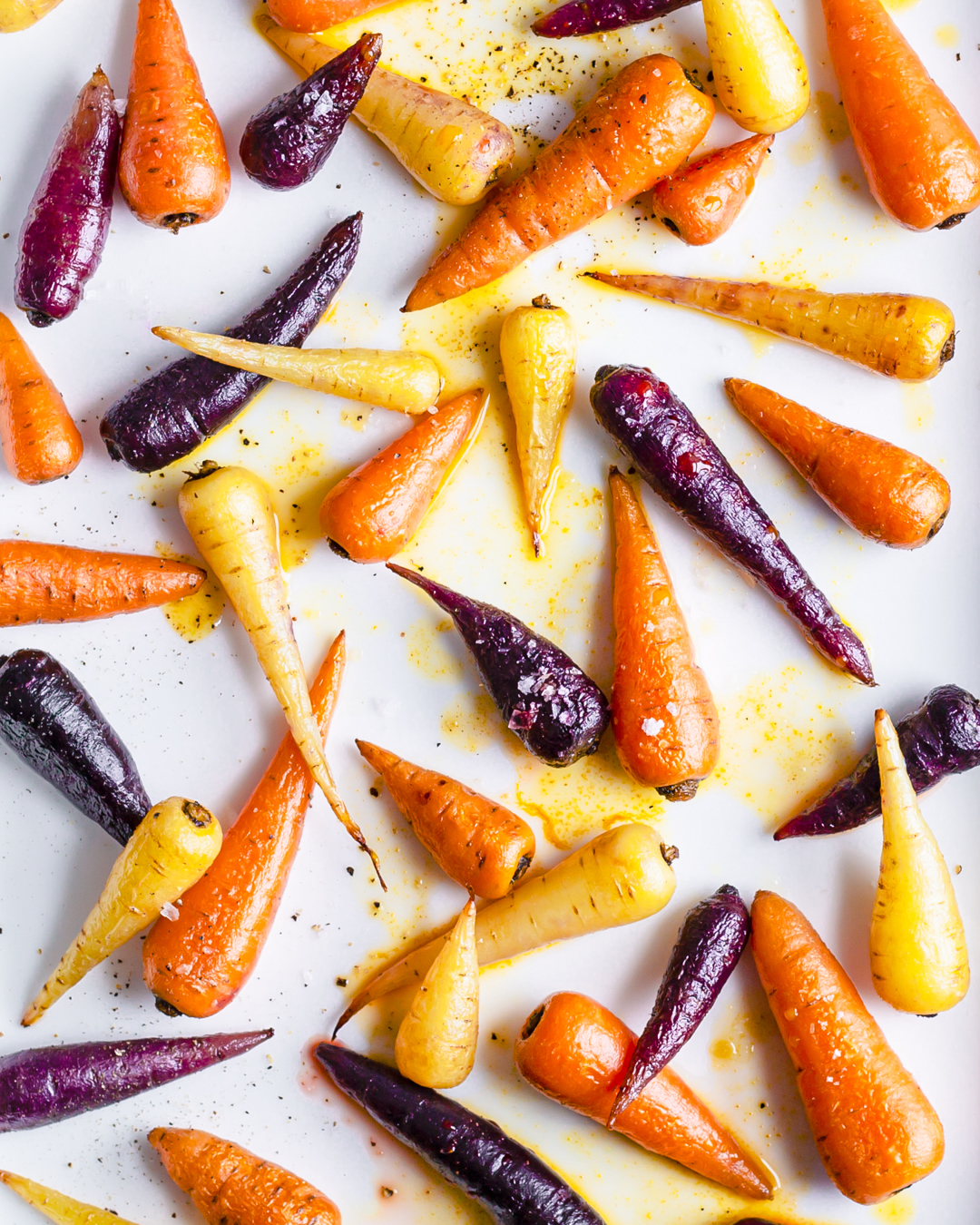 Overhead shot of colorful carrots on a white surface, orange, yellow, and purple variations, highlighting natural food photography.