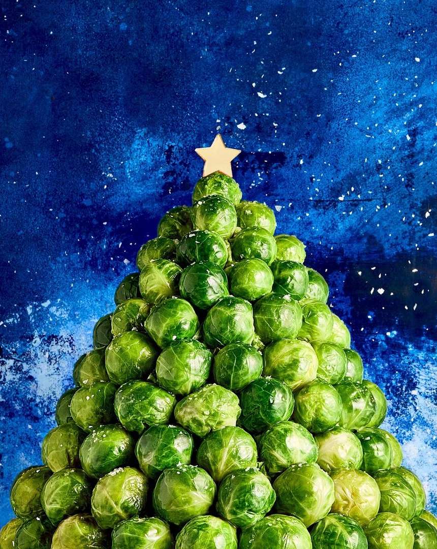 Festive Christmas tree crafted from Brussels sprouts, topped with a star, set against a textured blue backdrop speckled with white.