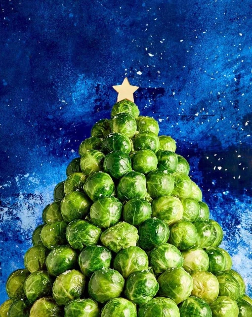Festive Christmas tree crafted from Brussels sprouts, topped with a star, set against a textured blue backdrop speckled with white.
