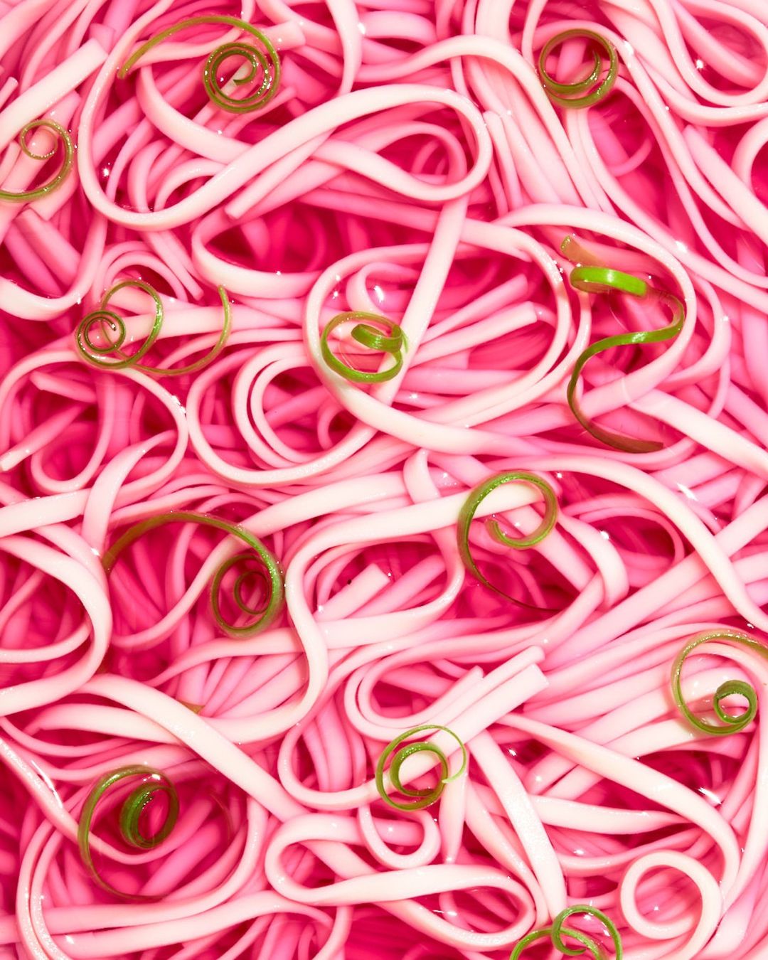 Overhead shot of bright pink noodles, garnished with green onions, creating a vibrant, textural food photography background.