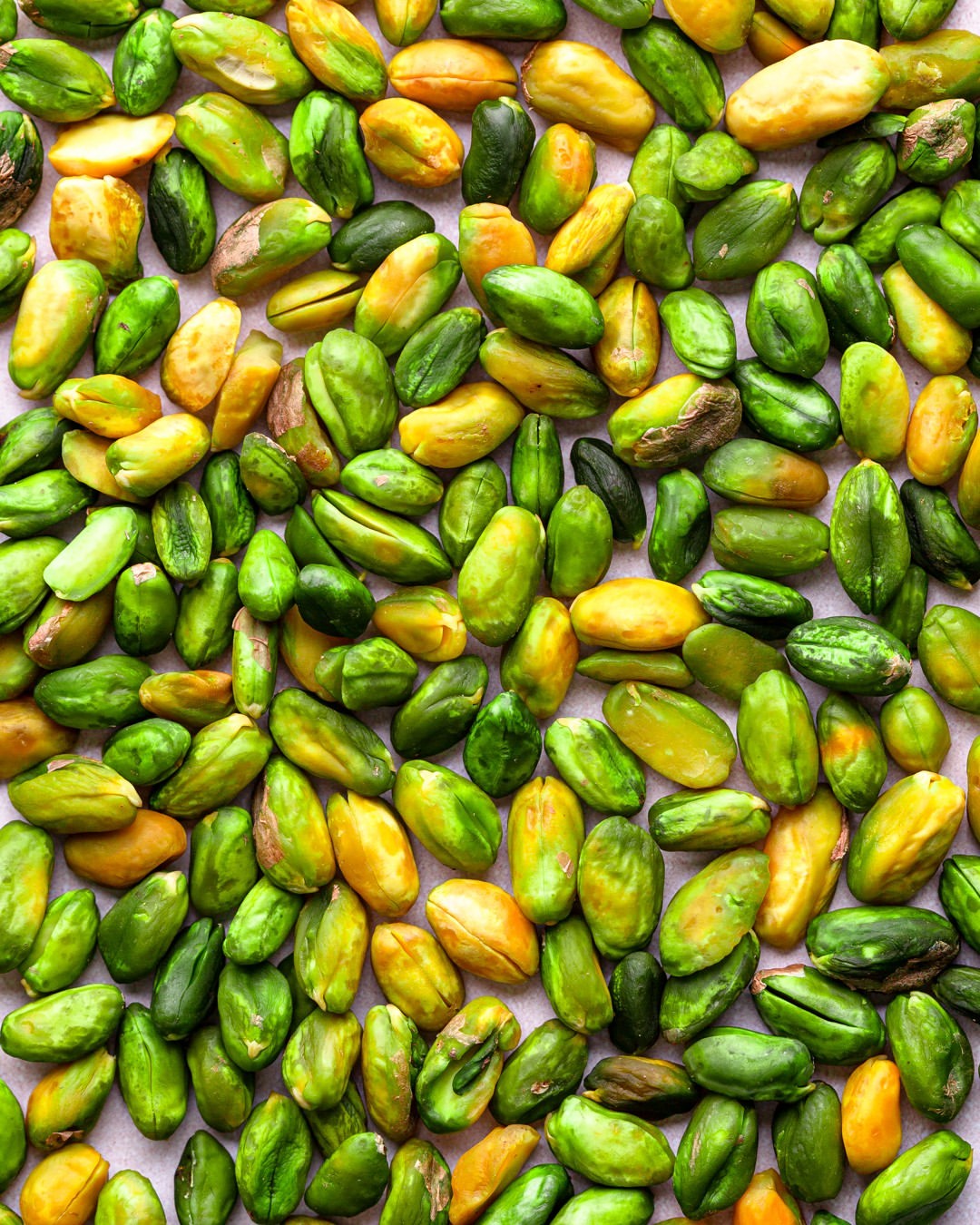 Overhead close-up featuring a dense arrangement of shelled pistachios in shades of green and yellow, creating a visually rich texture.