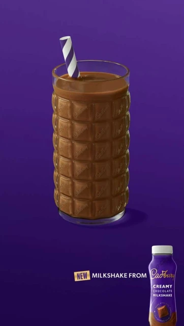 Tall glass filled with chocolate milkshake with striped straw next to bottle of milkshake against purple backdrop in studio lighting.